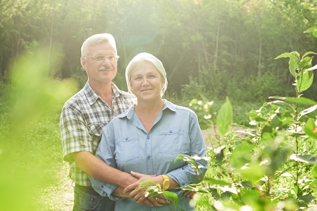 An elderly couple in love on a romantic date in a summer park smiling and hugging against a background of green trees