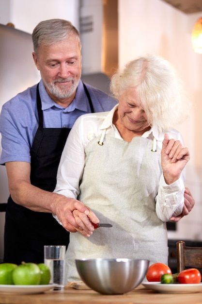 elderly couple preparing vegetable salad in kitchen, gray-haired handsome man helps wife with cooking, going to have healthy breakfast