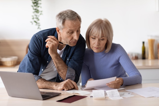 Elderly couple sitting at table using laptop paying bills