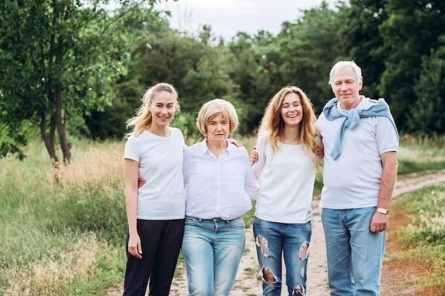 An elderly couple walks with adult daughters in nature. Mature couple walks in the woods. A family in white t-shirts and jeans is walking in the park. Happy family. family communicates outdoors