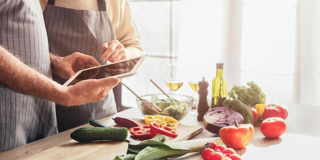 Photo an elderly couple wearing aprons stand in their kitchen looking at a tablet together kitchen is cozy