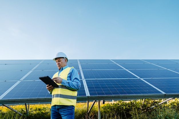 Elderly engineer is checking with tablet an operation of sun and cleanliness on field of