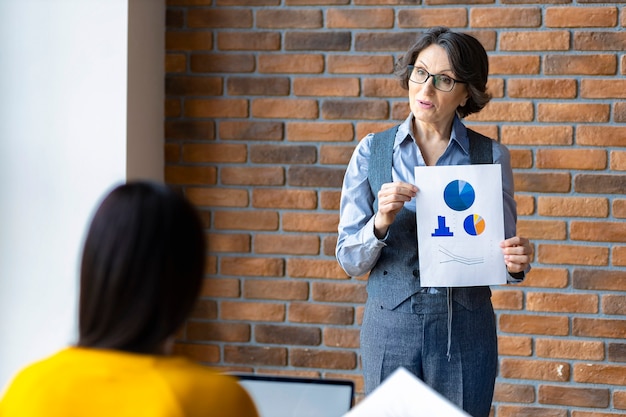 Elderly female mentor leader teaching employee analyzing sales or explain new business strategy at office meeting