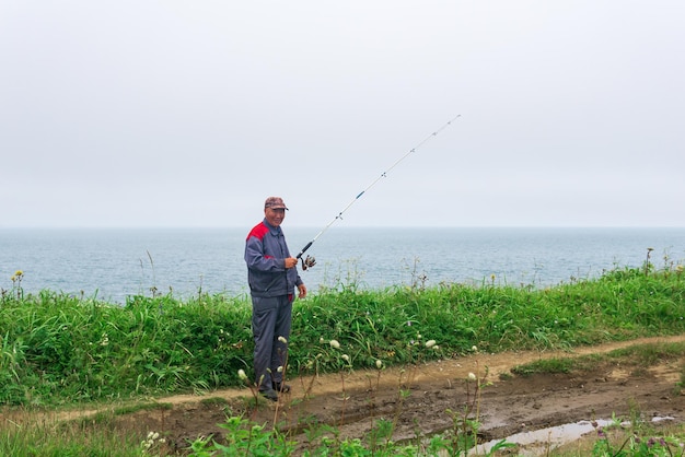 Elderly fisherman checks his fishing rod on the seashore