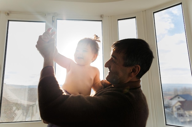 An elderly grandfather holds a small grandson in her arms and plays with him happy senior old adult