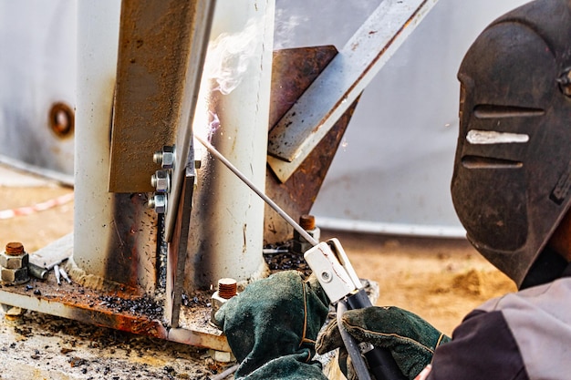 An elderly grayhaired grayhaired welder assembles metal structures at a construction site Arc welding work Sparks from welding Closeup