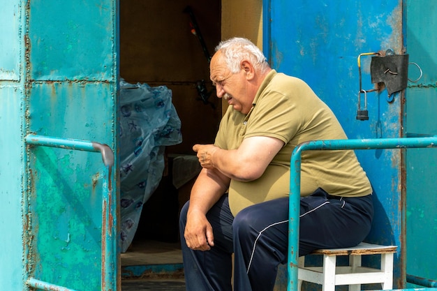 An elderly grayhaired man is sitting on a chair and holding his hand in the area of the heart Grandpa has heart problems Obesity and heart pain in old age