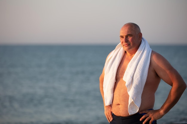 Elderly handsome man with a white towel on a background of the sea