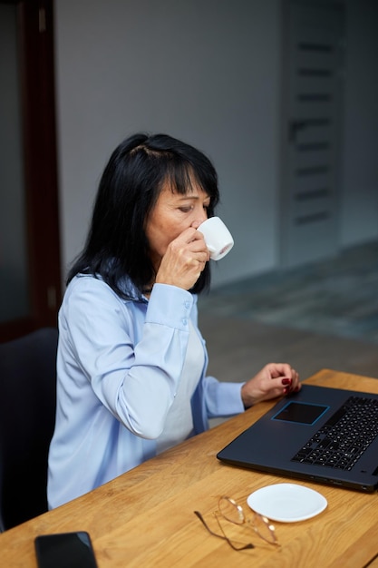 Elderly lady businesswoman relaxing at workplace drinking coffee