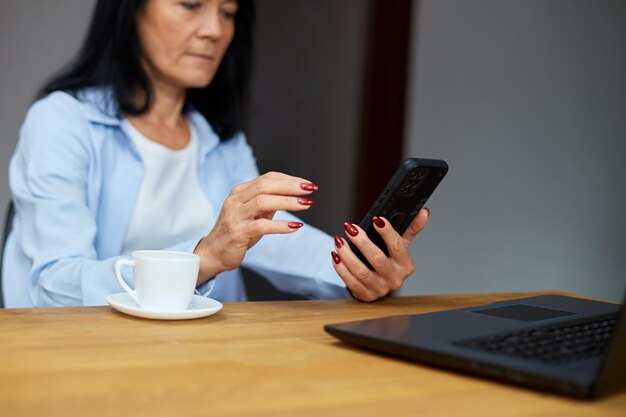 Elderly lady businesswoman relaxing at workplace using mobile phone