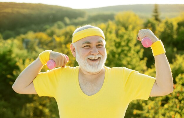 Elderly man after her workout happy senior sportman exercising with lifting dumbbell on green park b