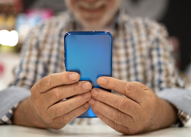 Elderly man in checkered shirt sitting at indoor cafe table using mobile phone senior caucasian male enjoying tech and social