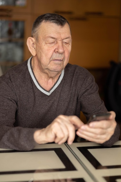 Elderly man dials number in smartphone from home Old senior sends sms on mobile phone