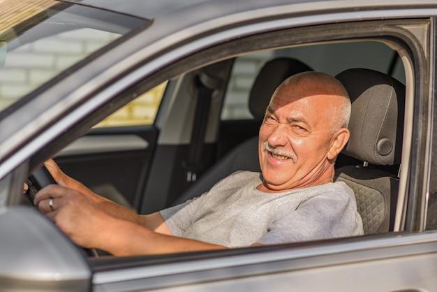 Elderly man driving a car, looking at the camera. driving or old age concept.