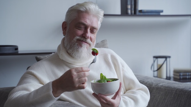 Elderly man feel happy enjoy eating diet food fresh salad on sofa