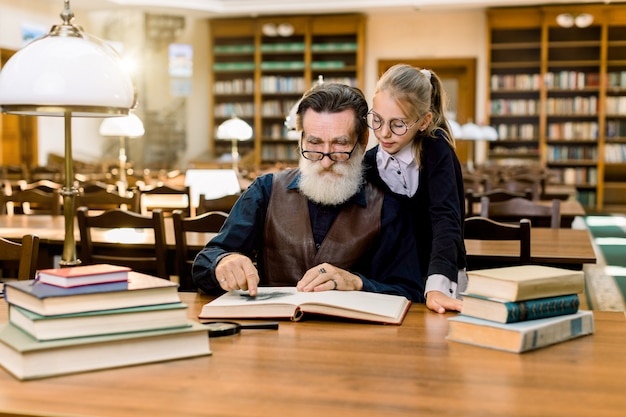 Elderly man grandfather and his granddaughter reading exciting book together in vintage old library