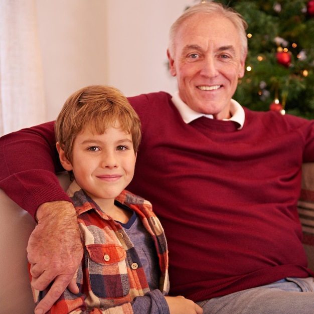 Elderly man grandson and christmas portrait on sofa with love bonding or happiness in family home Boy grandfather and smile together for celebration holiday or happy on couch in house by tree