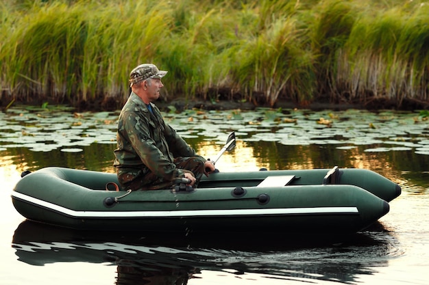 An elderly man is sailing on a rubber boat with oars on a calm river The inspector checks the reservoir from poachers