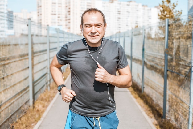 An elderly man runs on the street.