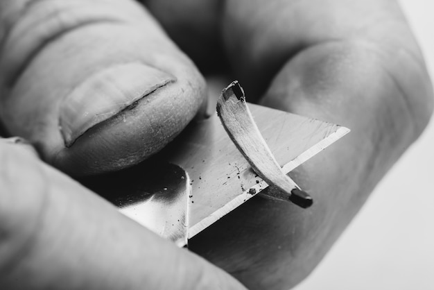 Photo elderly man sharpens pencil with clerical knife. fingers of artist close up in grayscale.