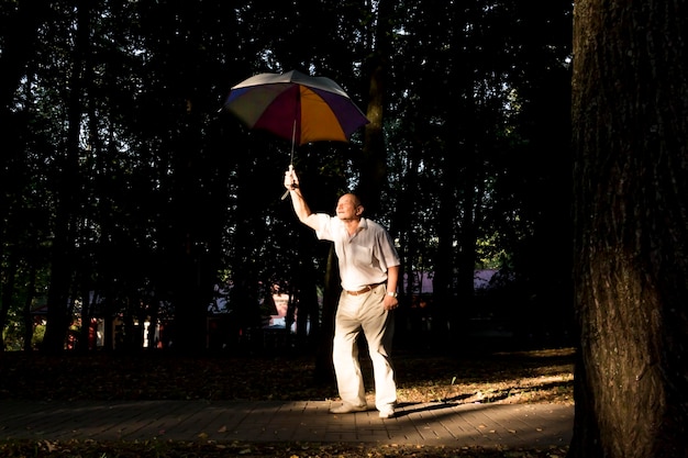 An elderly man stands under a large multicolored umbrella A pensioner on a walk in the park