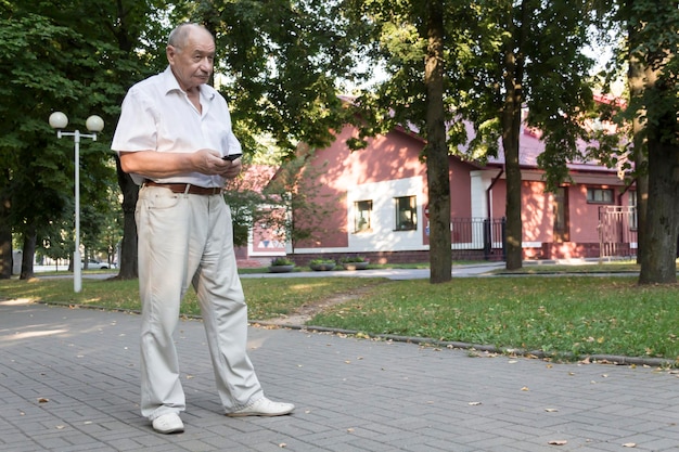 An elderly man walks alone in the park in the summer a modern retired businessman in a white shirt a