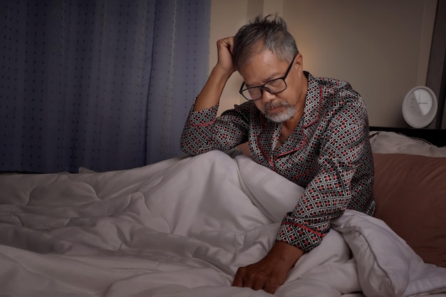 An elderly man with a depressed and stressed white beard sat in bed from insomnia