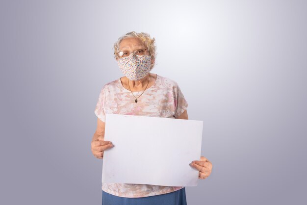 Elderly and masked woman holding a white sign on gray