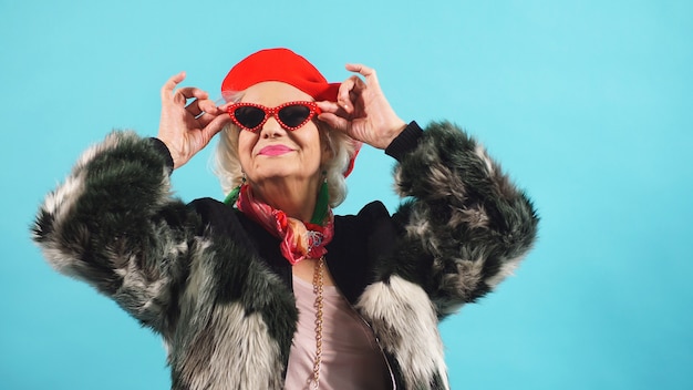 an Elderly pretty pensioner in a red hat and sunglasses poses  