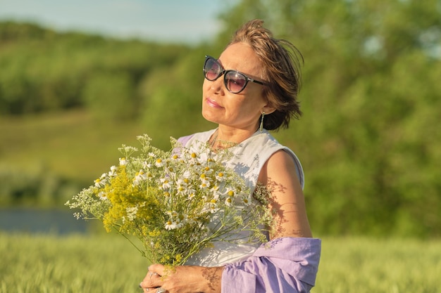 Photo elderly but still attractive asian woman breathing in the scent of a wild flower in a bright sunny