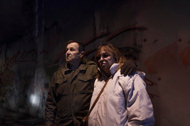 Elderly wife and husband standing together in an abandoned nuclear shelter