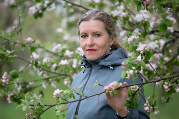 An elderly woman in a blooming garden looks at the camera