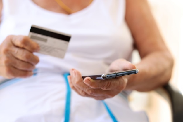 Elderly woman checks finances on credit card with smartphone online payment for pensioners