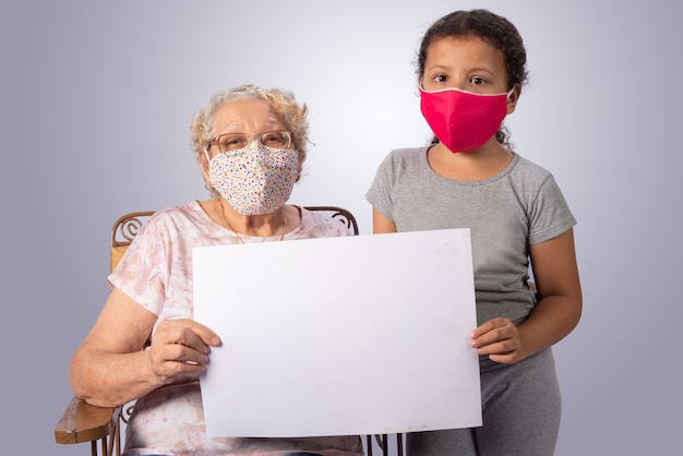 Elderly woman and child together in mascara holding a white sign on gray