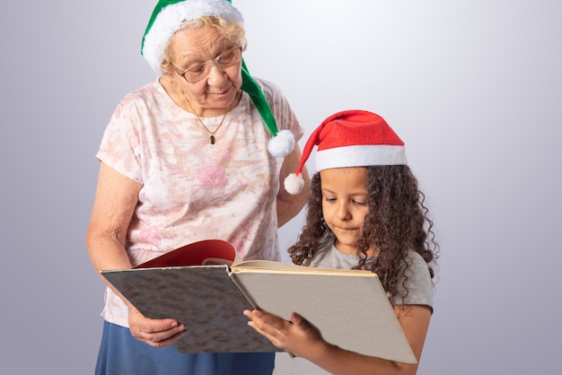 Elderly woman and child with Christmas hat reading a book on gray