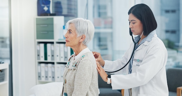 Elderly woman doctor and stethoscope on back to listen to lungs for breathing problem Senior medical professional and person with cardiology tools for exam consultation and healthcare in hospital