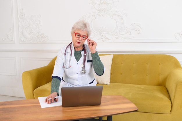 Elderly woman doctor works at the computer telemedicine doctor talking to patient using laptop high ...