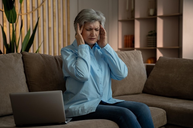 Photo elderly woman experiencing a headache while working on her laptop at home