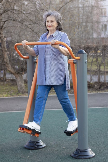 An elderly woman in the fresh air goes in for sports on the simulator Grandma is doing exercises