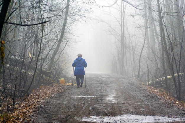 An elderly woman goes into the foggy distance along a dirty road