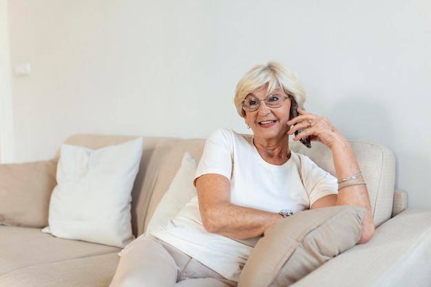 Elderly woman grandmother with gray hair sits at home on the couch using mobile phone a telephone conversation to hear the bad news Emotion fear scare