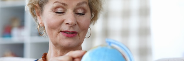 Elderly woman hold blue globe in her hand and point to continent with her index finger