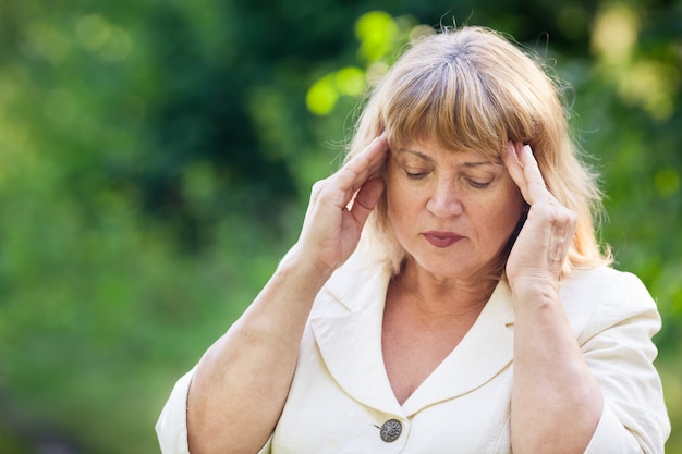 Elderly woman holds her head with fingers