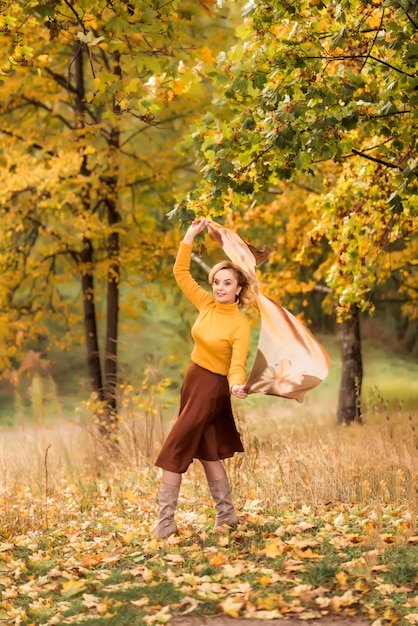 An elderly woman is spinning in an autumn park against a background of yellow leaves. Enjoying life.