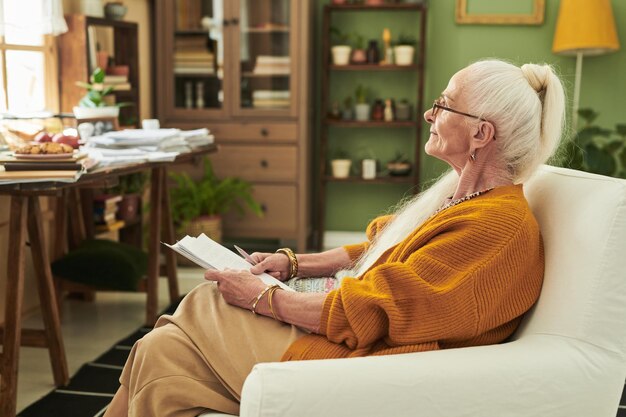 Elderly woman reading book in cozy living room setting