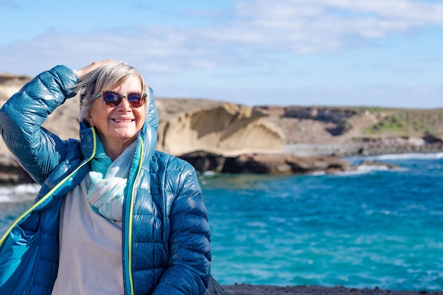 elderly woman at sea in winter day standing on the cliff  appreciating freedom and beauty in nature