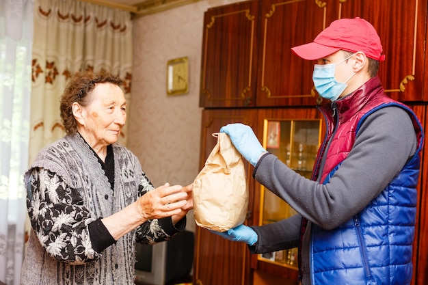 An elderly woman stays at home. Food delivery in a medical mask to the elderly.