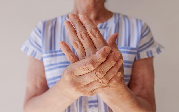 An elderly woman suffering from pain in her hand rubs her wrist closeup