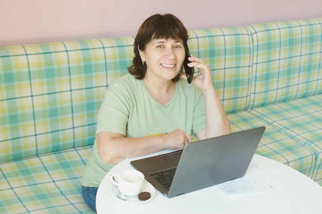 Elderly woman at a table with a laptop talking on a mobile phone