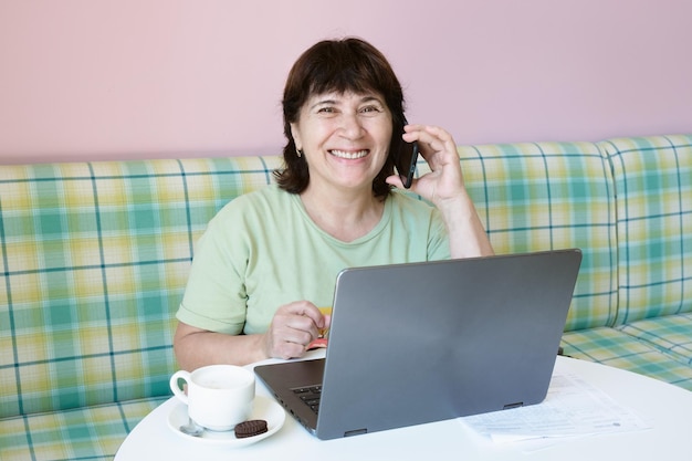 Elderly woman at a table with a laptop talking on a mobile phone